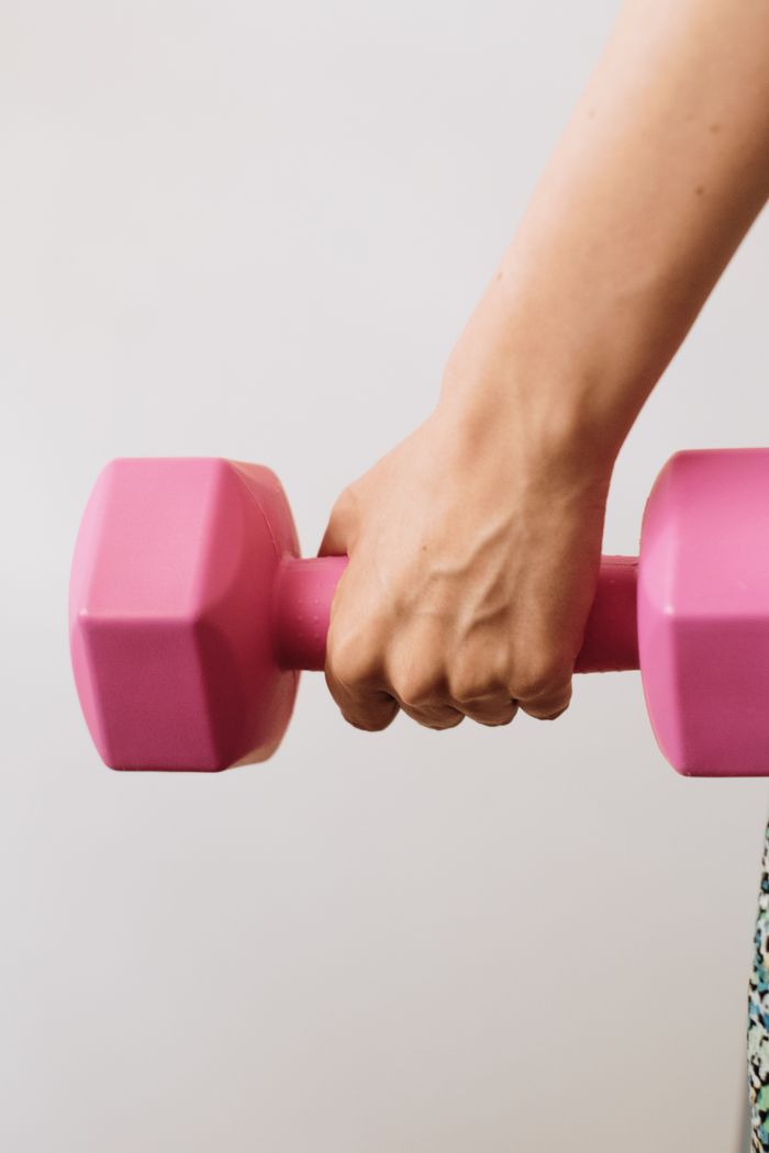 contact-img Close-up of person holding a pink dumbbell, signifying strength and fitness health.