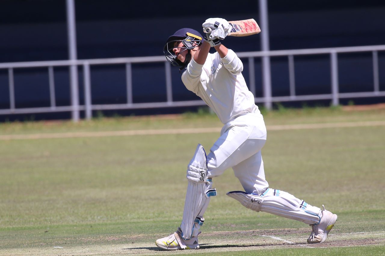 about-01 Cricketer in action hitting a shot on an outdoor field during a sunny day.