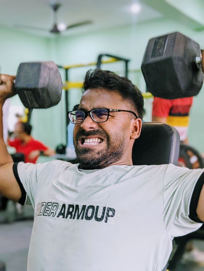 services-img Focused man lifting heavy dumbbells in a gym setting, showing determination and strength.