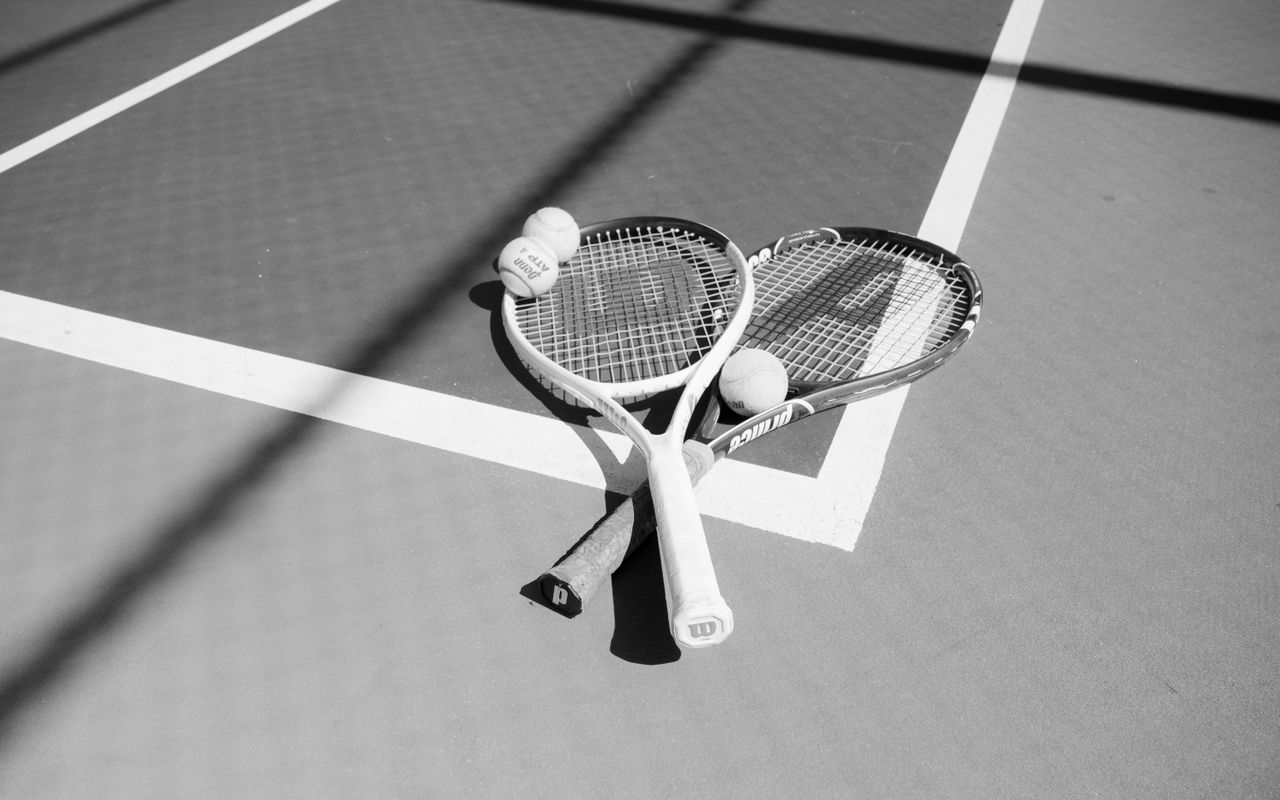 services-02 Monochrome image of two tennis rackets and balls on a sunlit court.