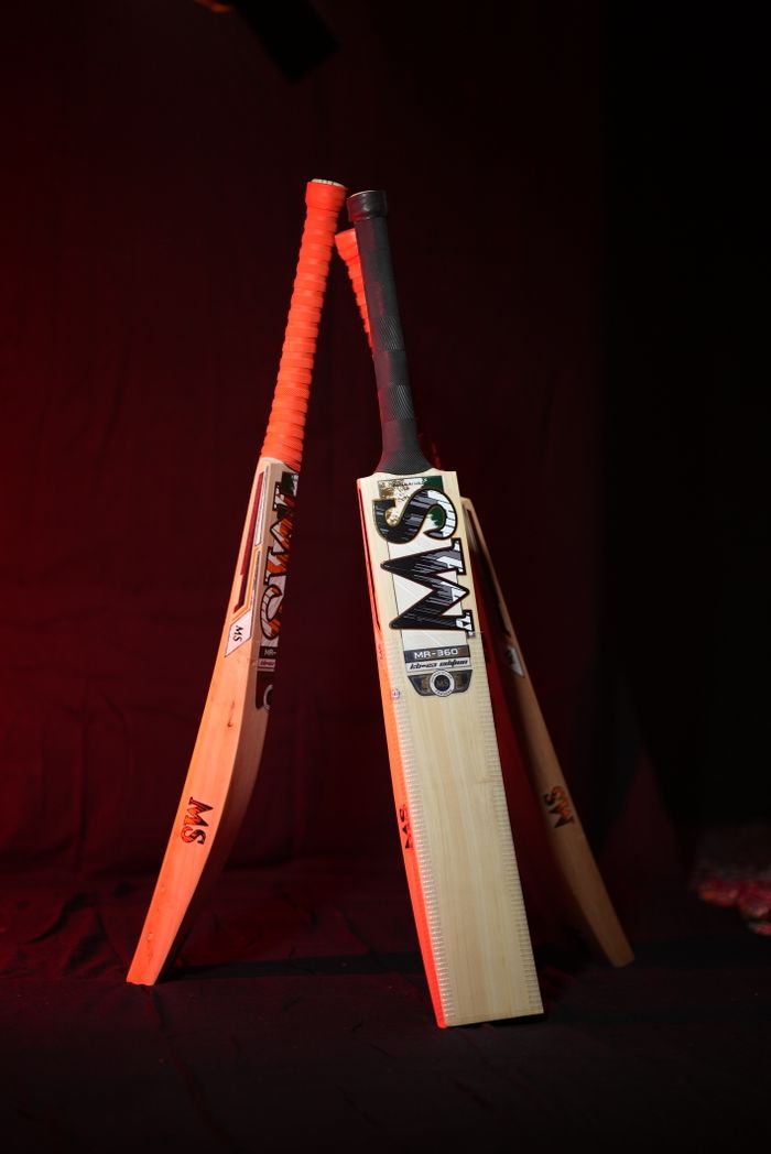 hero-img-01 Dynamic shot of three cricket bats illuminated with bold red lighting, creating a dramatic sports scene.
