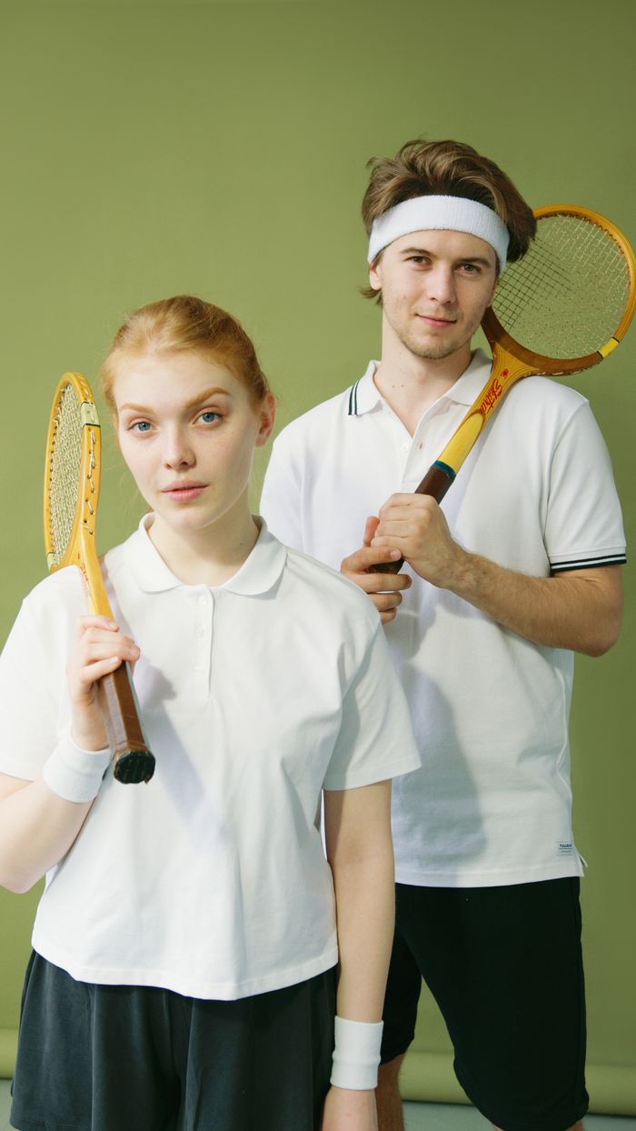 about-02 Young male and female squash players posing with rackets against a green background.