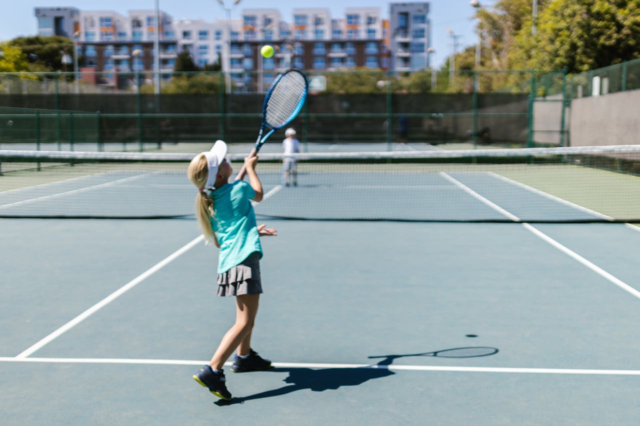 gallery-2 A girl in sportswear hitting a tennis ball on a sunny outdoor court.