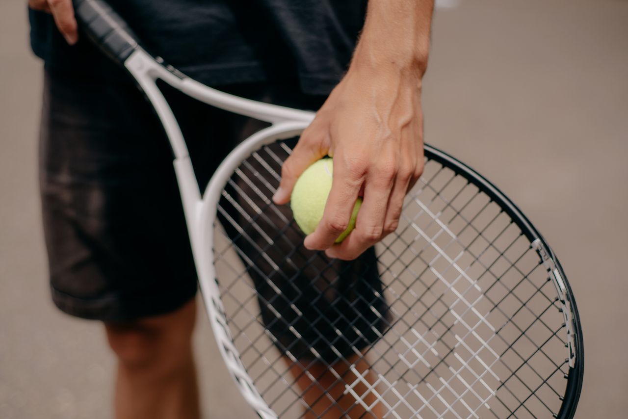 gallery-3 Detailed view of a tennis player holding a tennis ball and racket, preparing for a serve.